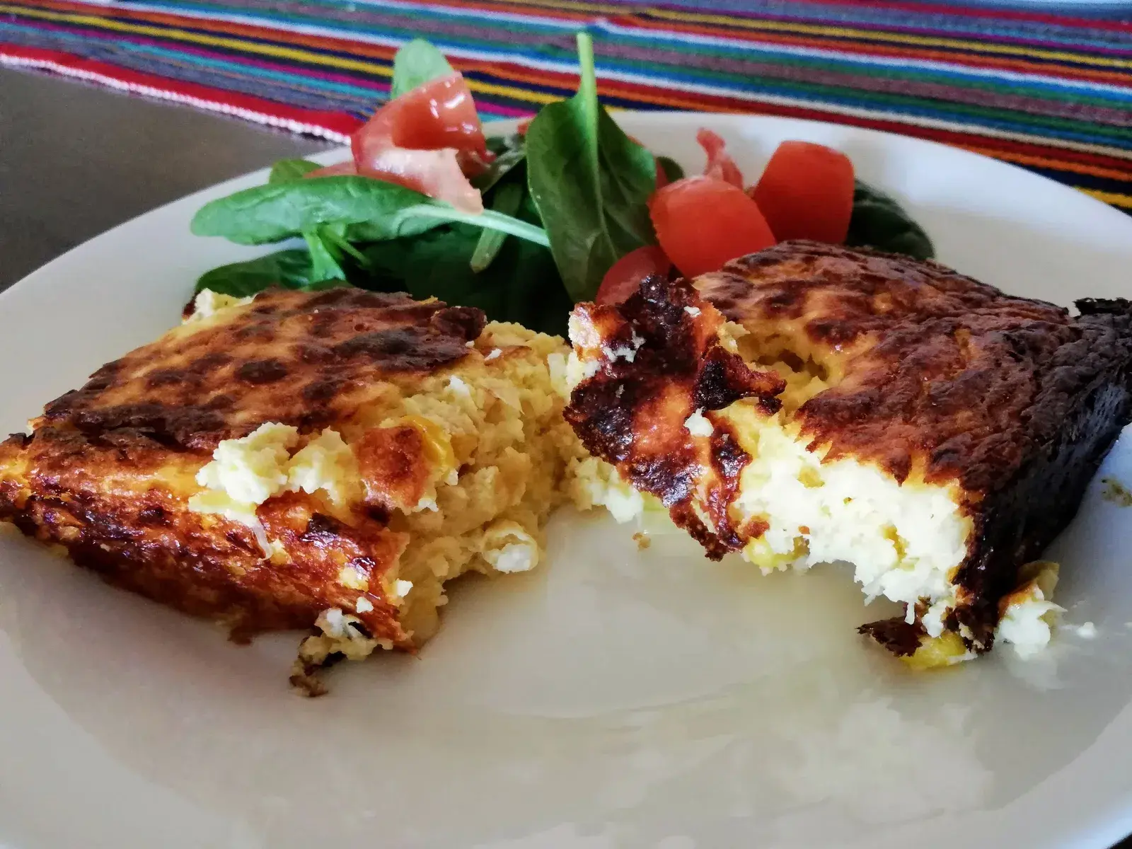 Twee porties chipa guasu met een goudbruine korst naast een salade, een klassiek bijgerecht van de Paraguayaanse keuken