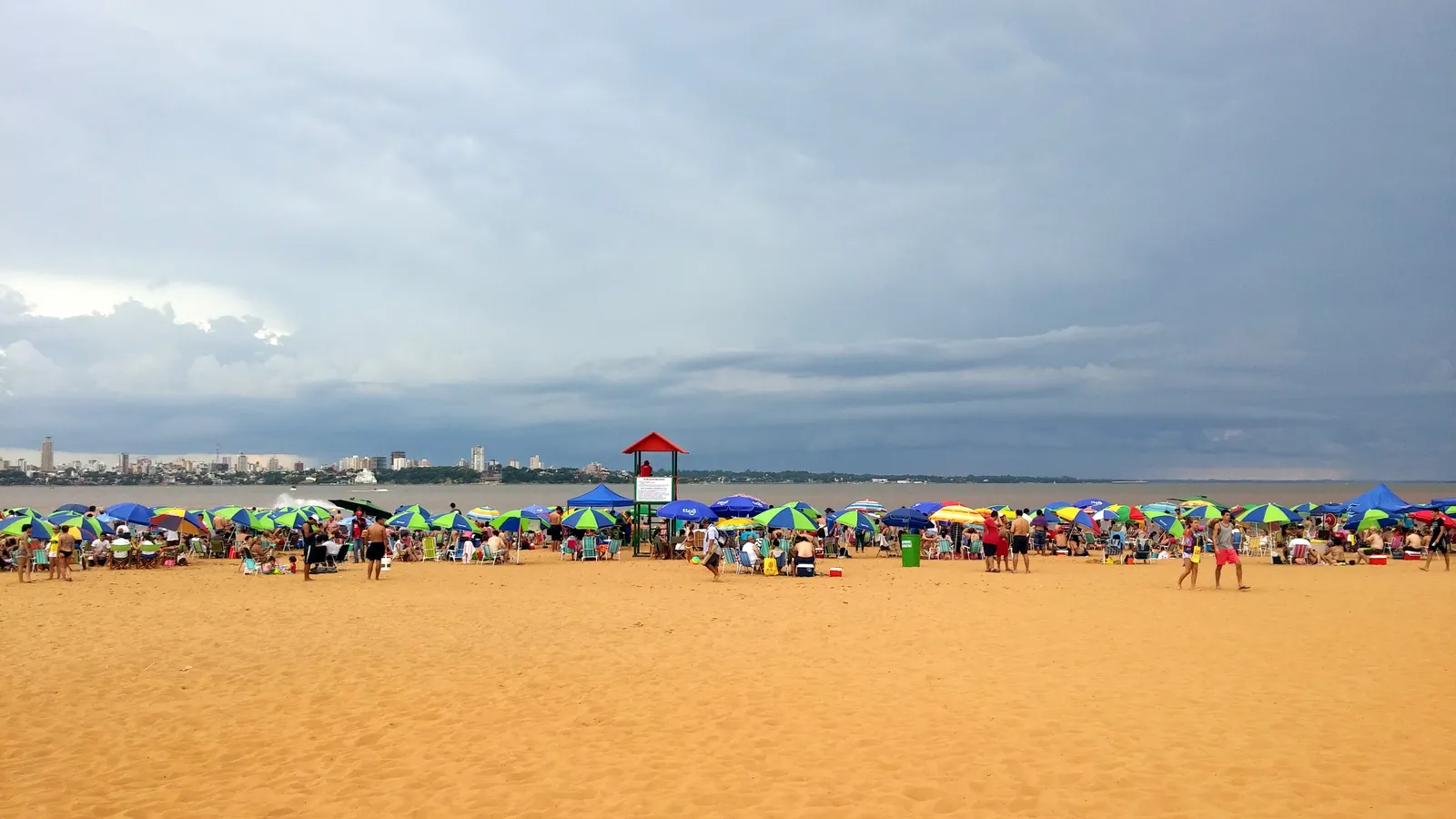 Gezinnen met kinderen onder parasols op het stadsstrand Playa San José in Encarnación, Paraguay